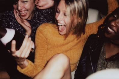 Young women laughing at a party while holding a bottle of alcohol.