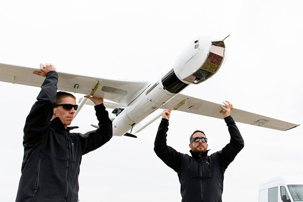 Two men holding a UAV by its wings.
