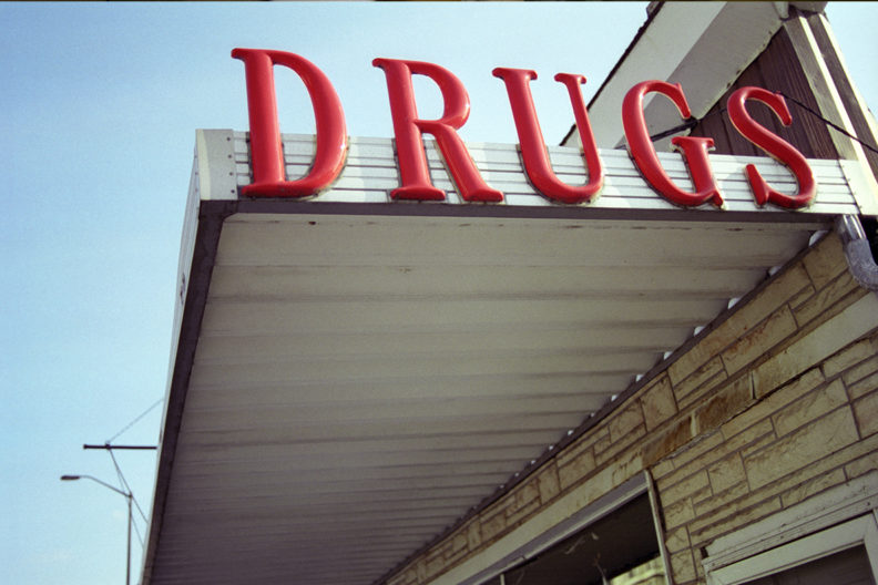 A photograph of an awning with the sign DRUGS in big red letters