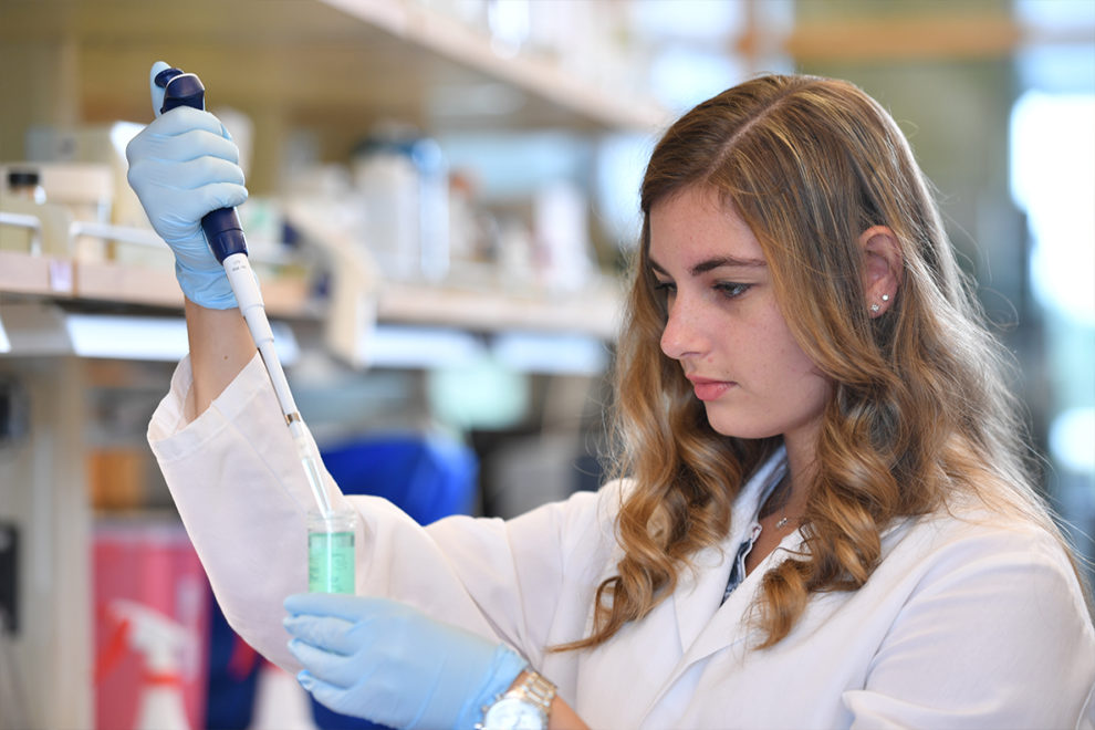 A female scientists drops a chemical solution into a beaker.