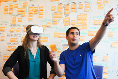 Two students in front of a white board with stickers on it.