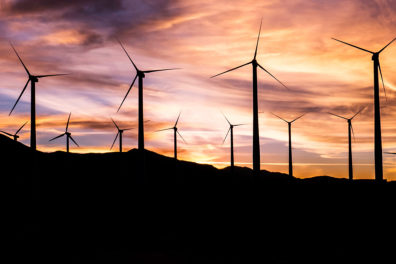 Several windmills stand on a hillside during sunset.