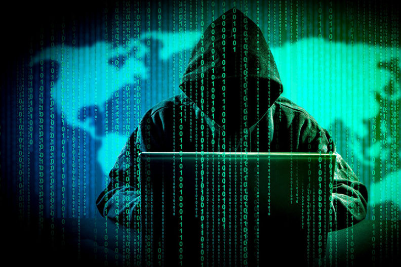A hooded figure at a computer in front of a map with binary digits dropping down in front