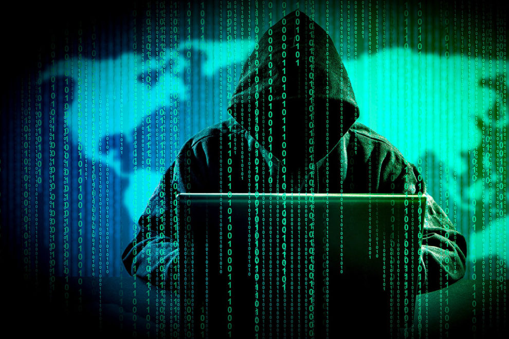 A hooded figure at a computer in front of a map with binary digits dropping down in front