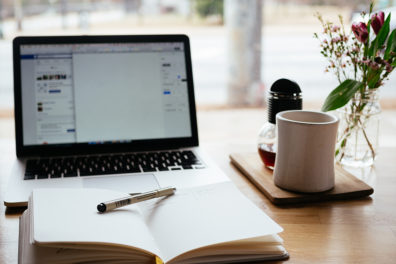 A laptop sits open with a notebook and pencil in front of it