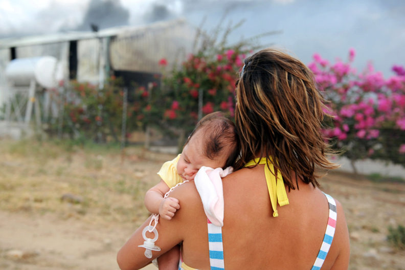 A young mother holding her sleeping baby as she watches their farm shed burn down.