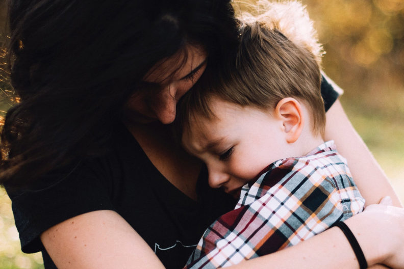 Sad woman holding sad boy closely in her lap