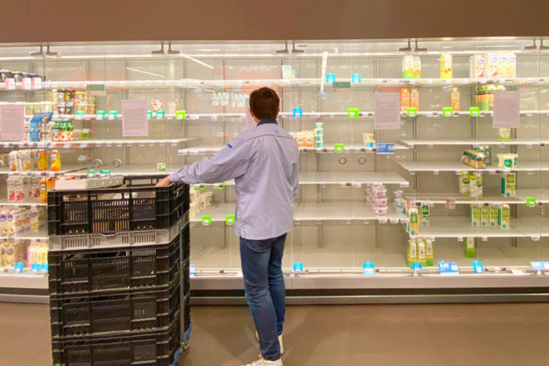 A grocery employee stands in front of several near-empty shelves.