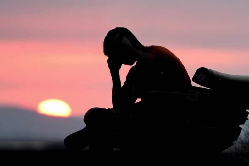Silhouette of young man on bench with his head on his hand.
