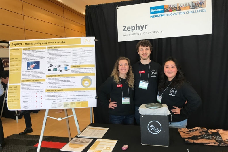Three students stand behind their invention at a poster competition