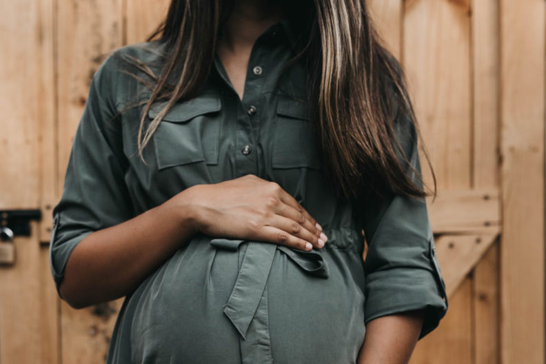 Pregnant woman in green shirt standing before wooden door