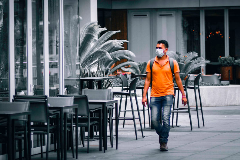 A man wearing a mask walks past closed businesses.