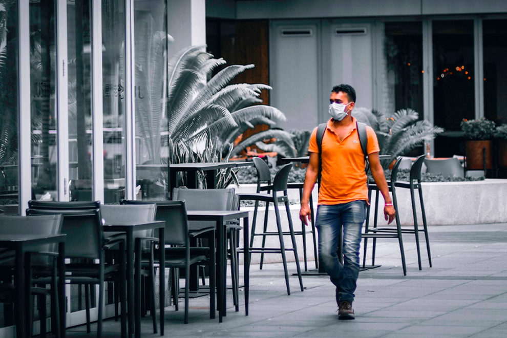 A man wearing a mask walks past closed businesses.