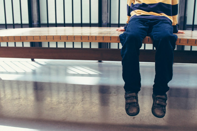 A child's legs dangling off the end of a bench in a juvenile center.