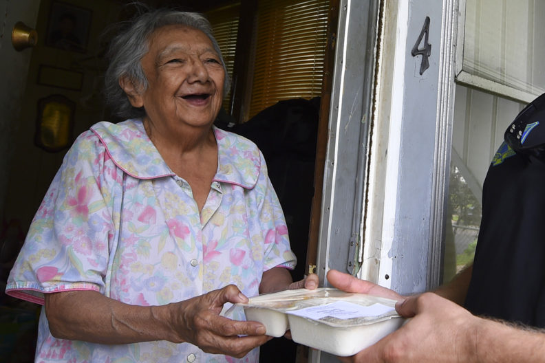 An elderly woman receives a Meals on Wheels delivery.