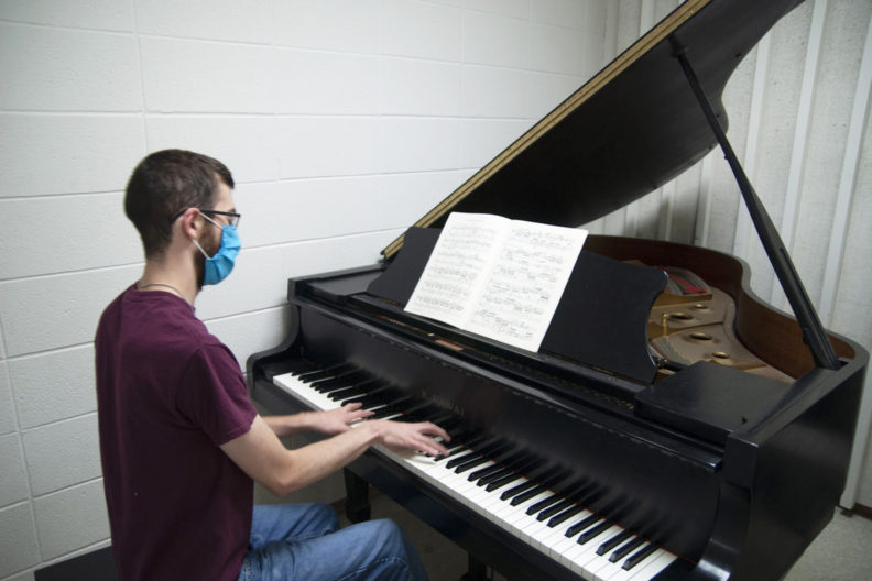 Graduate student Joel Lininger practices piano while wearing a face mask.