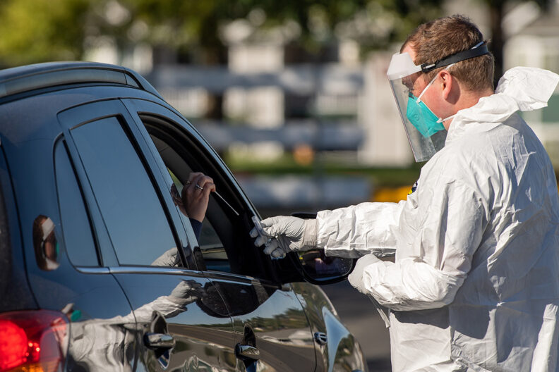 A National Guard member standing beside a car conducting COVID-19 testing.