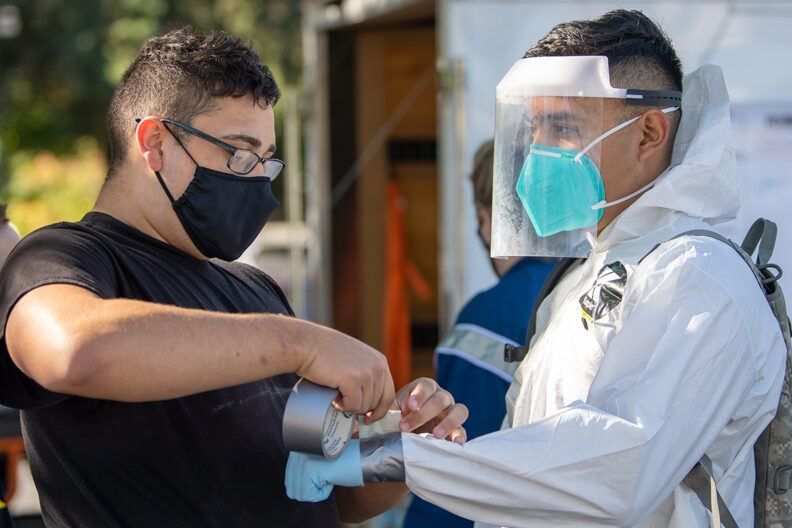 Someone duct tapes the sleeves of a protective suit for a National Guard member.