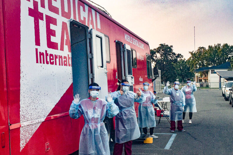 Students in PPE stand outside a mobile medical unit.