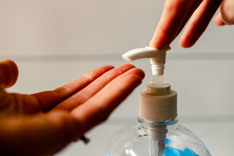 Closeup of two hands using a hand sanitizer dispenser.