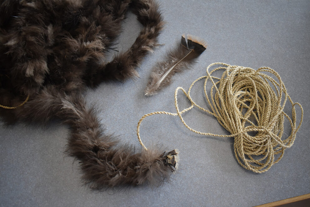 A segment of fiber cord that has been wrapped with turkey feathers, along with a single downy feather.