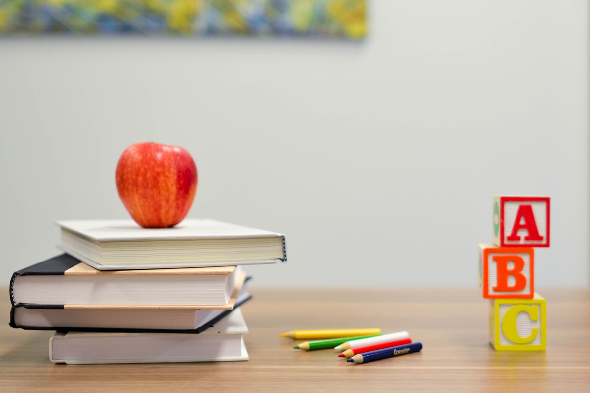 A stack of books with an apple on top next to colored pencils and a stack of ABC blocks