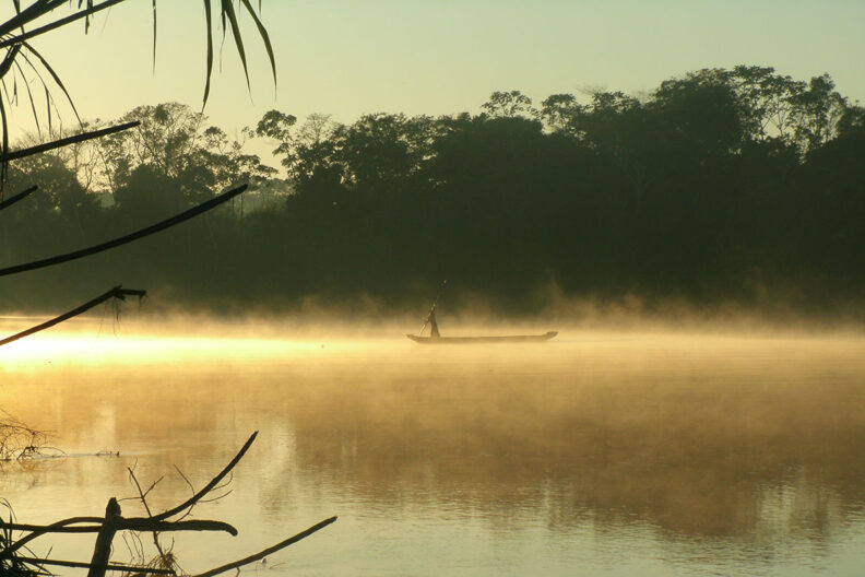 A person standing on a canoe with a pole as golden mist comes off the river water