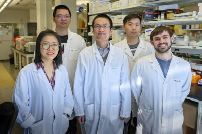 Five people in white lab coats standing in a lab.
