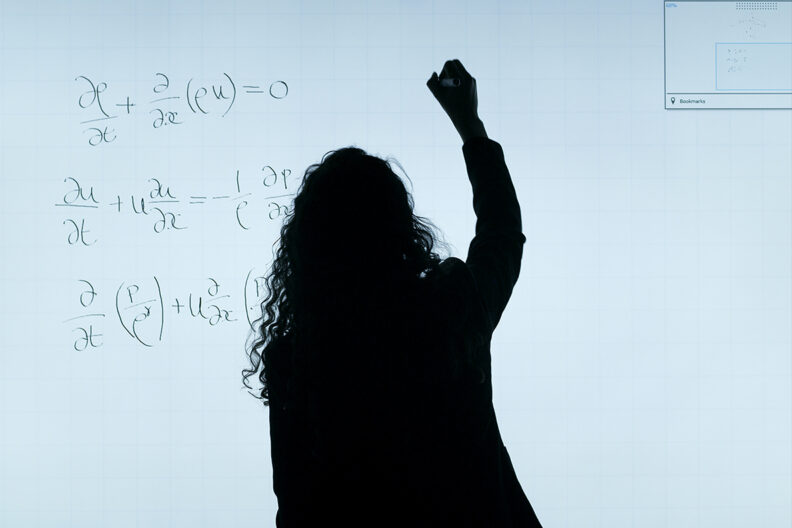 A math teacher writes on a white board