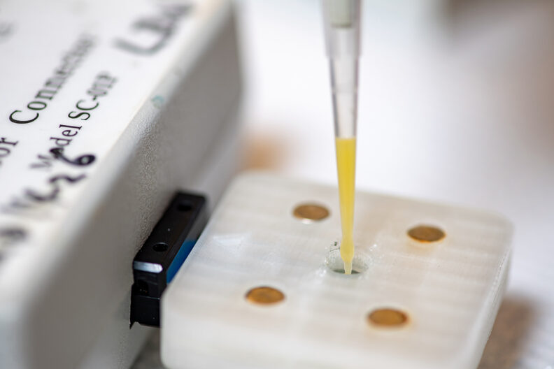A thin pipette of orange juice inserted into a plastic square sensor.