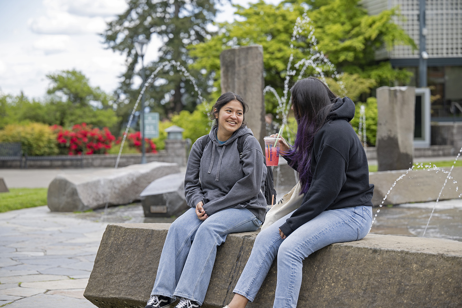 Dos estudiantes sonrientes conversan sentados en una fuente en WSU Vancouver.