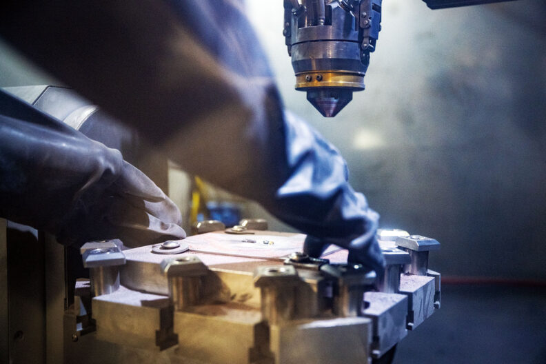 Gloved hands move the platform of a large 3D printer